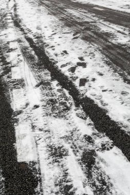 Lastik izleri ve ayak izleri olan karlı bir yol. Yol karla kaplı, lastik izleri ve ayak izleri var.