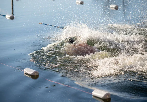 Suda beyaz bir şamandırayla havuzda yüzen bir adam var. Şamandıra bir ipe bağlı.