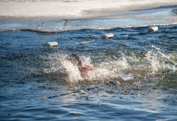 Bir adam okyanusta yüzüyor ve su sıçrıyor. Su soğuk ve adam dalgıç kıyafeti giyiyor.