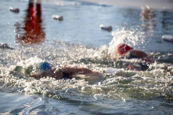 İki yüzücü suda, biri mavi bir başlık takıyor. Su sıçrıyor ve yüzücüler oradan geçiyor.