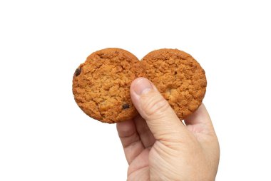 Bir çiftte iki kurabiye tutan bir el. Kurabiyeler kahverengi ve çikolata parçacıkları var. Hoşgörü ve haz kavramı. Kurabiyeleri elinde tutan kişi, onları yemeye hazır.