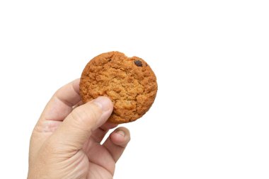 Isırılmış kurabiyeyi tutan bir el. Kurabiye kahverengi ve çikolata parçacıklı.