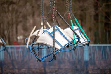 A row of swings hanging from a chain. The swings are blue and white. The swings are old and rusted