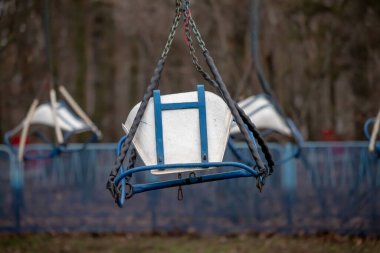 A blue and white swing is suspended from a chain. The swing is empty and he is in a park
