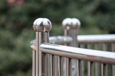 A metal railing with a silver finish and a few round balls on top. The railing is surrounded by trees and bushes, giving it a natural and peaceful feel