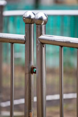 A metal fence with two silver balls on top of it. The fence is surrounded by a green area