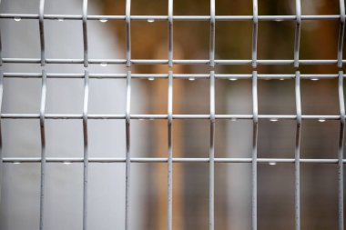 A close up of a metal fence with a white background. The fence is made of metal and has a grid pattern