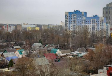 Arka planda mavi bir bina olan bir şehir manzarası. Evler küçük ve ağaçlar çıplak.