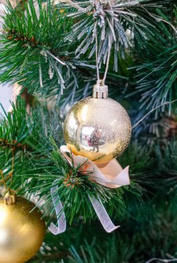 A gold ornament hangs from a Christmas tree. The ornament is shaped like a ball and has a ribbon attached to it. The tree is full of green leaves and the ornament is the only decoration on it
