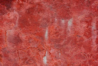 A red wall with a rough texture. The wall is covered in dirt and has a few cracks
