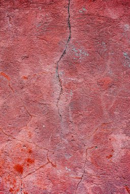 A red wall with cracks and a rough texture. The wall is old and worn, giving it a sense of history and character