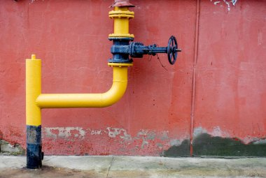 A yellow pipe with a black cap is attached to a wall. The pipe is connected to a gas line