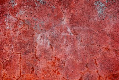 A red wall with a rough texture. The wall is covered in small holes and has a faded appearance