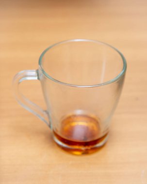 A glass cup with a brown liquid in it sits on a wooden table. The cup is half full, and the liquid appears to be a type of tea. Concept of relaxation and comfort