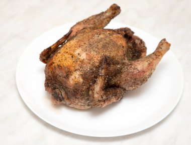 A roasted chicken is sitting on a white plate. The chicken is covered in spices and he is cooked to perfection. Concept of warmth and comfort