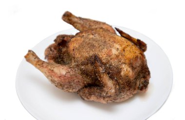 A roasted chicken is sitting on a white plate. The chicken is covered in spices and he is cooked to perfection. Concept of warmth and comfort, as the chicken is a popular