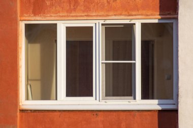 A window with a white screen and a red wall behind it. The window is open and the sunlight is shining through it