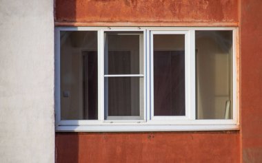 A window with a white frame and a white screen. The window is on a building with a red wall