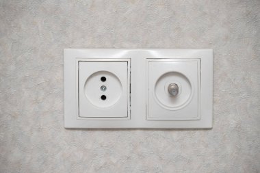 A white wall with a white switch on it. The switch is a two pronged outlet