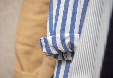 Bir kişi mavi beyaz çizgili çizgili bir gömlek giyiyor. Gömlek duvarda asılı.