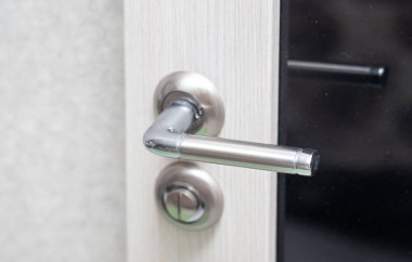 A silver door handle with a green button. The handle is attached to a door that is closed