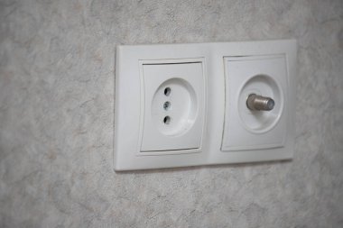 A white wall with a white outlet on it. The outlet is white and has two holes