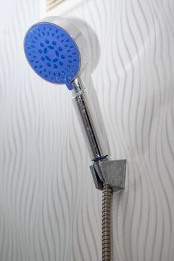 Mavi başlıklı bir duş başlığı. Duş başlığı duvara yapışmış.