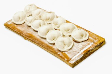 Üzerinde mantı yığını olan tahta bir tahta. Hamur köfteleri beyaz ve pişirilmeye hazır görünüyorlar.