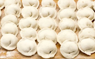 Tahta bir masada çok sayıda hamur köftesi oturuyor. Hamur köftelerinin hepsi aynı boyutta ve şekildedir, ve hepsi beyazdır. Masa un ile kaplı.