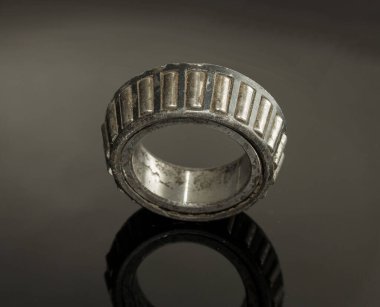 A worn out, rusted, and dirty bearing is sitting on a black surface. The bearing is a part of a machine and has been used for a long time. Concept of wear and tear