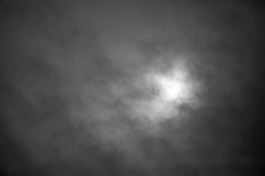 Bulutların arasından süzülen parlak güneşli bulutlu bir gökyüzü. Gökyüzü karanlık ve karamsar, ama güneş bir umut ve sıcaklık hissi getiriyor.