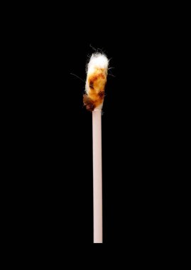 A used Q-tip is shown on a black background. The Q-tip is brown and has a burnt tip