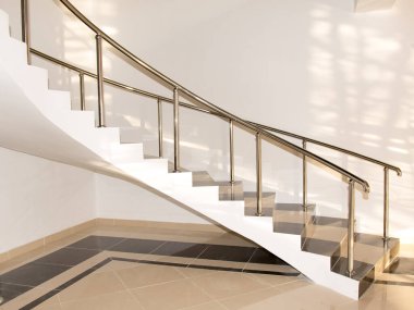 Metal parmaklıklı sarmal bir merdiven. Merdiven beyaz ve siyah. Korkuluklar gümüş rengi.