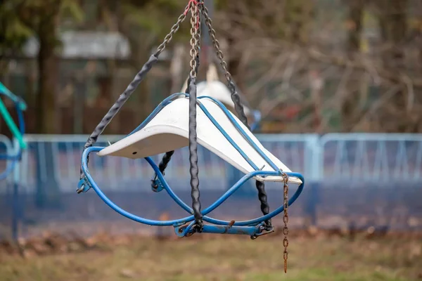 Üzerinde zincir sallanan mavi ve beyaz bir salıncak. Salıncak boş ve beyaz koltuğu var.