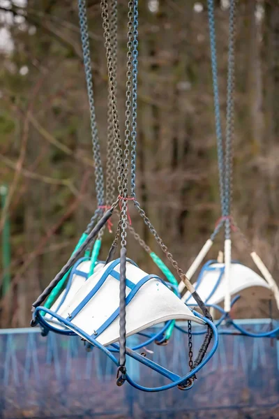 A couple of old swings hanging from chains. The swings are blue and white