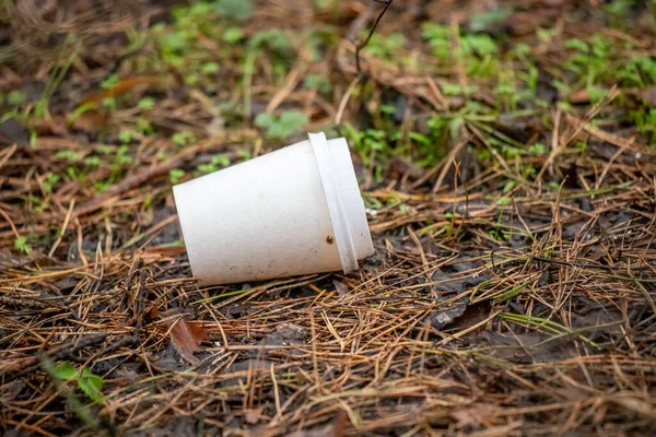 A cup is laying on the ground in a field. The cup is empty and has a lid on it. The field is covered in grass and leaves, and the cup is surrounded by dirt. The scene gives off a sense of abandonment