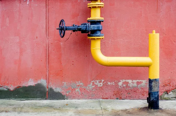 A yellow and black pipe is attached to a wall. The pipe has a black cap and is positioned in a way that it is not visible from the front. The wall behind the pipe is red and has some dirt on it