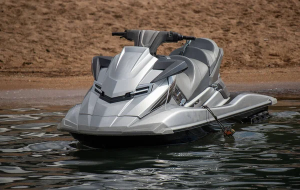 Suda gümüş renkli bir jet ski oturuyor. Su sakin ve gökyüzü berrak.