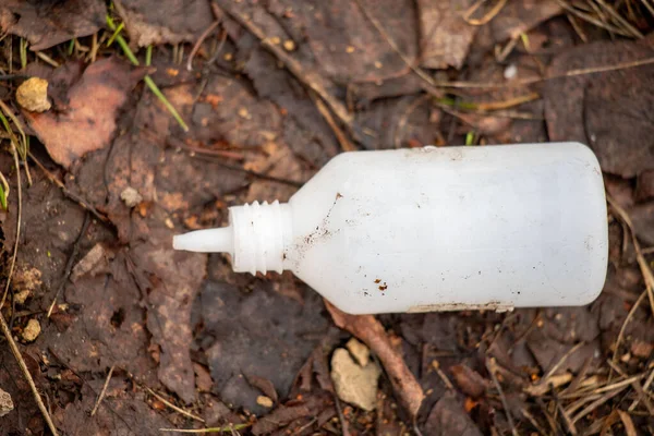 Yerde bir şişe bir şey var. Kirli ve kapağı var. Şişe bir toprak parçasının üzerinde.