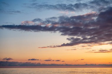 Gökyüzü mavi ve turuncu renklerin güzel bir karışımıdır, bulutlar etrafa saçılmıştır. Okyanus sakin ve huzurlu, sakin bir atmosfer yaratıyor.