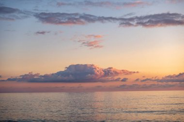 Gökyüzünde büyük bir bulutla okyanusun üzerinde güzel bir gün batımı. Gökyüzü pembe ve turuncu renklerin karışımıdır.