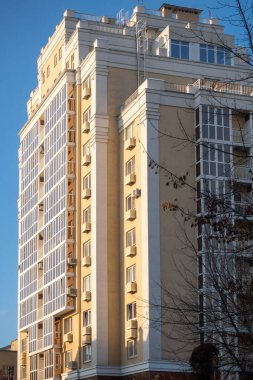 Bir sürü penceresi ve balkonu olan yüksek bir bina. Bina kahverengi ve beyaz. Gökyüzü mavi