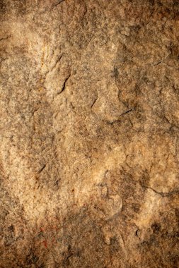 Kahverengimsi bir rengi olan bir kaya duvarının yakın çekimi. Duvar pürüzlü ve bir sürü dokusu var.