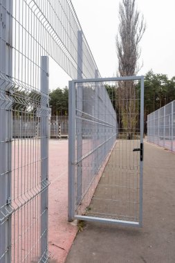 Çitin önünde bir kapı açık. Kapı metalden yapılmış ve siyah bir sapı var.