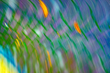 Yeşil ve mavi arkaplanlı, turuncu ve sarı çizgili bulanık bir görüntü. Görüntünün hareket ve enerji duygusu var, sanki hareket halindeymiş gibi.