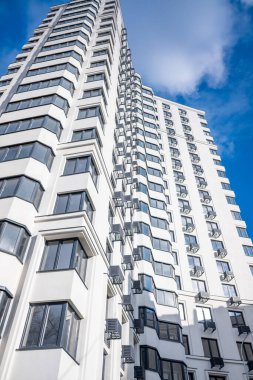 Arka planda mavi gökyüzü ve birçok penceresi olan uzun beyaz bir bina. Bina çok uzun ve modern görünümlü.