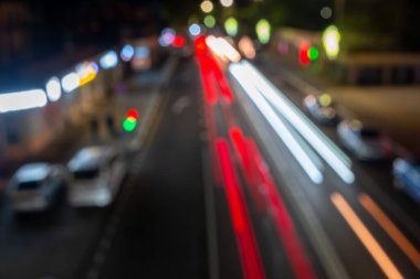 Gece kalabalık bir caddenin bulanık bir görüntüsü. Arabaları ve otobüsü var. Arabalardan ve sokak ışıklarından gelen ışıklar hareket ve enerji hissi yaratıyor.