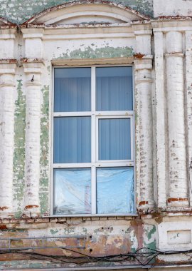 Mavi perdeli ve beyaz çerçeveli bir pencere. Pencere yeşil ve beyaz yüzlü bir binanın üzerinde.