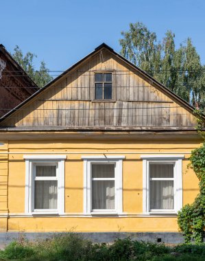 Üç pencereli ve ahşap çatılı sarı bir ev. Ev eski ve kırsal bir havası var.