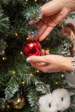 Bir insan Noel ağacına kırmızı bir süs asıyor. Kişi, süsü elinde tutuyor ve ağaca doğru bakıyor. Sıcaklık ve tatil ruhu kavramı